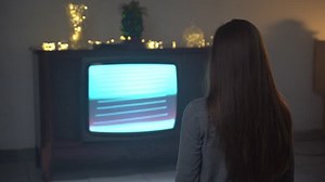 Problem of TV addiction of modern society, woman sitting on the floor in dark room and watching broken retro TV screen with flicking stripes, distortion and bad signal interference of vintage