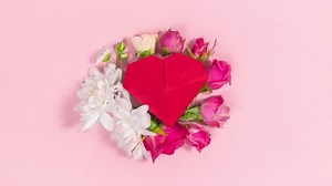 4k Red origami heart sways, decorated with natural flower buds. Pale pink background. Concept of valentine's, mother's day holiday, wedding and and other occasions. Looped stop motion animation.
