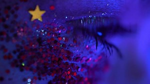 Extreme closeup woman blinks, tear flows from eye. Female with stage makeup illuminated neon light