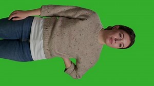 Vertical video: Front view of close up young adult greeting person with wave, smiling in studio. Relaxed casual woman waving hi or hello on camera, standing over full body green screen background and