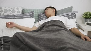 Asian male restless sleeper nearly waking up in the morning is tossing and turning on bed in the bedroom at home.