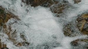 Seething water bubbles in waterfall close-up. Crystal clear water raning rapidly and forms foam with bubbles in mountain waterfall. Super slow motion. Rough water framed by stones. no people