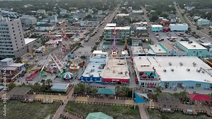 aerial footage of the Carolina Beach Boardwalk with a Ferris wheel, colorful amusement rides, people walking, a sandy beach, blue ocean, hotels and, condos at sunset in Carolina Beach North Carolina