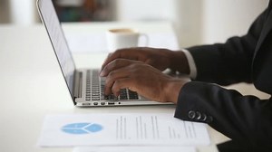 Black male hands typing on laptop keyboard at desk, african man in suit working on pc computer at home office, preparing e presentation or report considering project stats in documents, close up view
