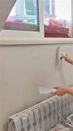 applying white putty smoothly on a concrete wall surface using a metal scraper tool indoor