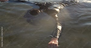 Drowned man with long dark hair in the water sways in the muddy water lying face down in shallow water. Unrecognizable body in black clothes is washed ashore after a shipwreck. 50 fps 4k slow motion