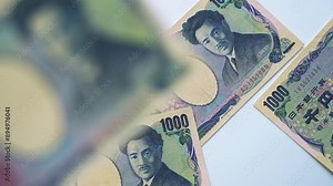 Falling Japanese Yen banknotes and pile of Japanese currency banknotes are spinning on table