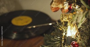 Record spins on a turntable in the background of a small decorated Christmas tree with glowing lamps on Christmas Eve