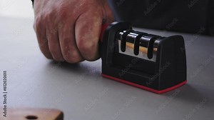 a kitchen knife and a person's hand is sharpened in a special sharpener for knives on the table. Slowmotion