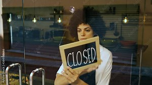 Businesswoman puts closed sign at the glass door of a bar or restaurant. Owner of a small business, people and crisis concept.