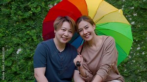 4K, Two Asian women of the same sex are sitting under colorful umbrellas symbolizing gender equality to live together happily. Both show their love for each other. Love and friendship of LGBTQ couples
