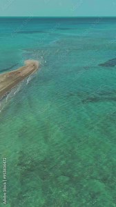 This video features a stunning aerial view of a sandbar in the ocean . The sandbar is a long, narrow strip of land that is exposed at low tide. The water around the sandbar is crystal clear and varies