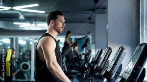 Sports man walking on treadmill in modern gym. Handsome man in black tank top having cardio to burn calories. Treadmill walking. Man is focused and determined. 4K, UHD