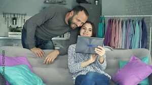 Young couple with tablet computer talking while sitting on sofa at home