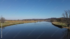 Wide landscape view of waterways in Wisconsin in autumn. Calm glistening water. Reflections from the sun on the water. Bare trees dotting the island. Patches of green grass