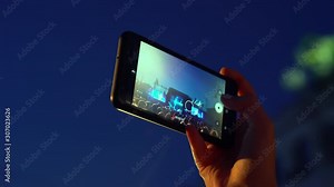 Happy people are watching an amazing musical concert. Merry fans jump and raise their hands up. Fans are filming a concert on a smartphone. Live concert.