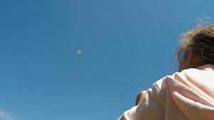 Kid playing with the flying kite. Little girl holds a flying kite. Colorful kite into the blue sky. Low-angle shot, 4K resolution, slow-motion