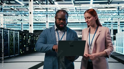 Engineering team in server hub working together with laptop to do maintenance tasks on machines. Teamworking colleagues in modern high tech data center configuring server settings, camera A