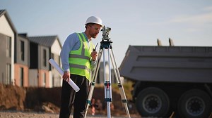 Surveyor using theodolite and walkie talkie on construction site