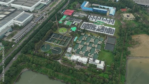 Top down drone footage flying over a large wastewater treatment facility with circular clarifiers and aeration tanks for water purification