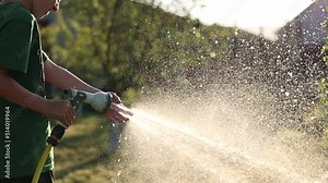 child plays with water hose sprinkler in the garden. Sunny Summer Day children playing in the backyard. In Slow Motion