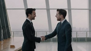 Two men in suits shaking hands and nodding in a happy manner