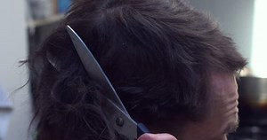 Man cuts his own hair with blunt scissors