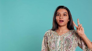 Jolly indian person doing peace victory hand sign gesture, studio backdrop. Portrait of upbeat woman, feeling confident, celebrating win, isolated over studio background, camera B