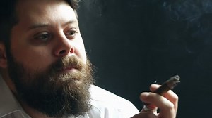 Handsome bearded man on serious face holding cigar in studio