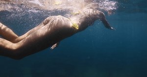 Woman in bikini swims underwater in clear blue lake