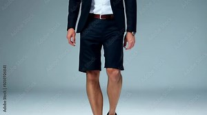 Male model wearing a blazer, white shirt, and tailored shorts, walking confidently in a minimalist studio setting