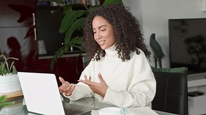 Young latin woman, female student or worker using laptop remote working at home office looking at computer talking at online meeting communicating by video call, elearning or having virtual interview.