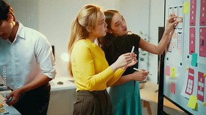 Team of ui and ux designers are working together in their office, using sticky notes and a whiteboard to brainstorm ideas for a new mobile application