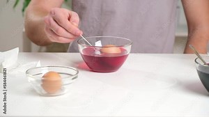 A man puts an egg on a spoon into a glass cup with a dye. Dyeing easter eggs with food coloring is the first step in favorite Easter egg decorating ideas. Stock Video