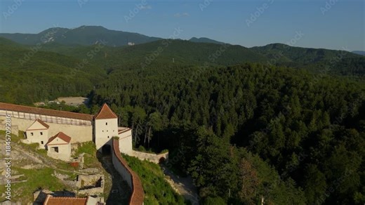 Rasnov Fortress, Transylvania – cinematic drone pullback reveal from partial view to wide panoramic aerial of the western side, exposing medieval citadel, forests and iconic RASNOV sign, Romania