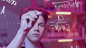 Young man solves mathematical equations on blackboard. Media. Young man solves complex equations on transparent board. Genius writes equations on blackboard in neon light