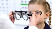 Optometrist examining girl eyesight using optical trial frame, vision...