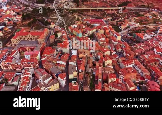 Aerial view shows a town with many houses and buildings. Red roofs cover the structures. Narrow streets connect homes in the area. The setting is rural and surrounded by hills Stock Video Footage - Alamy