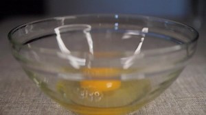 Egg yolk falling in slow motion into the bowl with another cracked egg.
