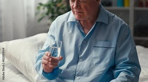 Sad man in his 70s taking pills with water, dealing with old age health issues, taking supplements