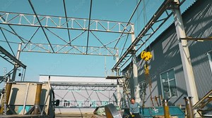 Technician worker using hoist crane for lifting metal detail in workshop factory. Creative. Work process and machinery.