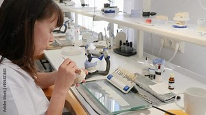 dental technician is applying ceramics with brush on teeth implants on workplace with tools and equipment in light workroom at job