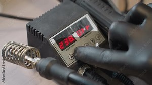 Close view of a gloved hand adjusting the digital temperature control on a soldering station, changing the temperature from 242 degrees to 238 degrees