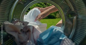Woman taking clean laundry out of a washing machine, with a green lawn in the background. View from inside the washing machine Stock Video