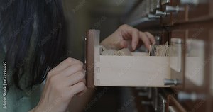 Close-up of female reader hand searching book in library catalogue working at educational project. Knowledge and college scholarship concept.