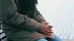 Closeup of hands rubbing together in cold winter. Anxious female nervously thinking about her problems. Woman in a jacket warming her fingers on a freezing day outside, sitting on a bench by the sea.