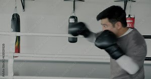 Side view of confident Asian boxer shadow fighting training alone in boxing ring concentrated on moves. Martial arts and sportsman concept.