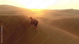 Drone, travel and man walking on desert sand dunes In Namibia on vacation or holiday. Aerial view, freedom and male outdoors on remote sandy, barren and dry wasteland on peaceful adventure