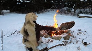 A wide view as a native warrior is seen worshipping spirits by a burning fire, wearing sacred wolf skin coat over head for peace, strength and courage