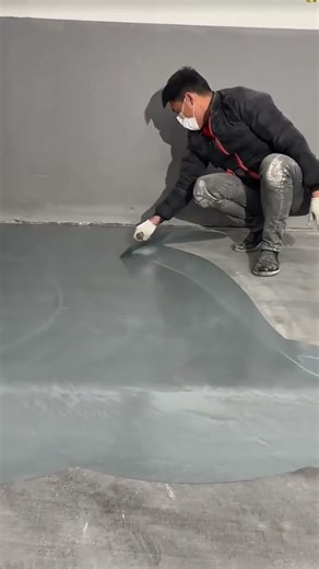 Worker applying liquid grey epoxy floor coating with squeegee